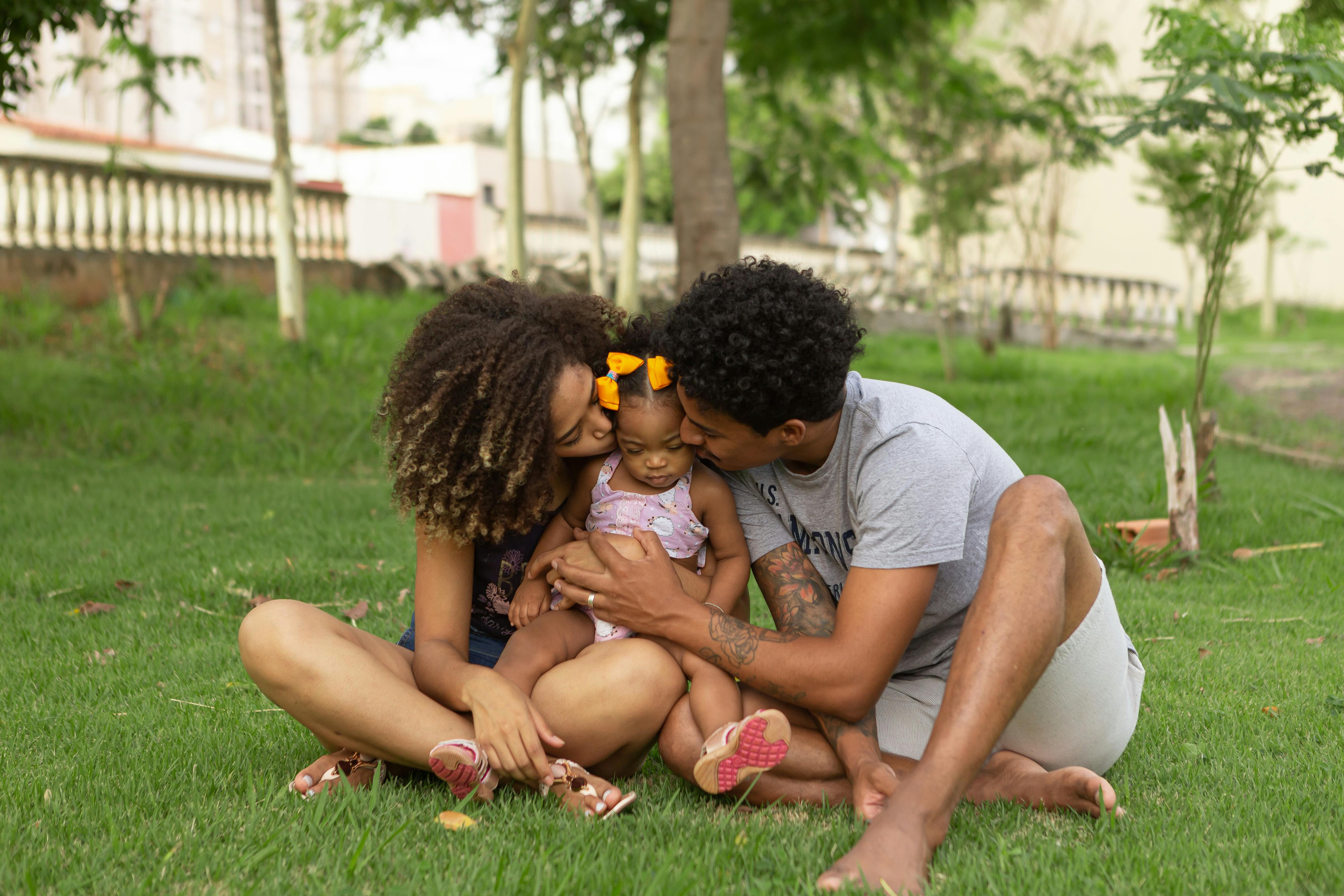 Family of three sitting on grass in a park.
